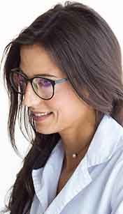 A woman with glasses smiling, wearing a white coat.