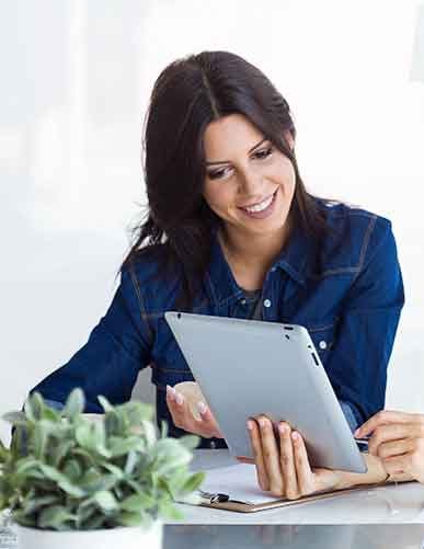 A woman smiling while using a tablet.